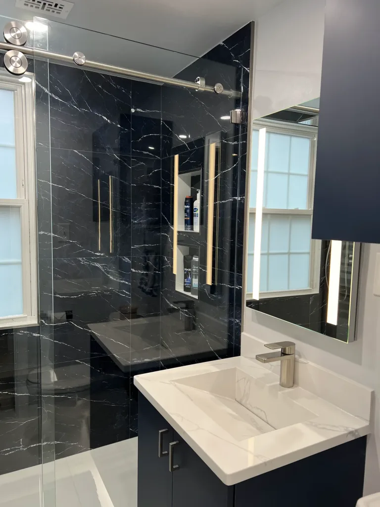 Spa-style bathroom remodel in Arlington, VA with a navy floating Millwork vanity, European integrated sink and black marble-look porcelain shower by Kitchen & Bath Masters