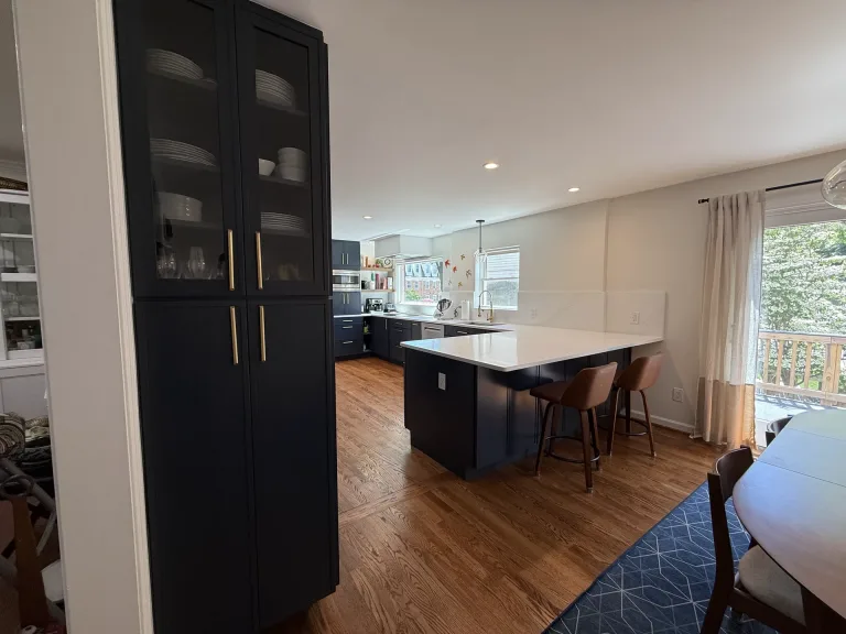Open-concept kitchen remodel in McLean, VA with a navy Waypoint glass-front pantry cabinet and white quartz island by Kitchen & Bath Masters