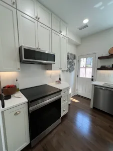 Range wall with Dove shaker cabinets, microwave hood and floating wood shelves in a remodeled Washington, DC kitchen