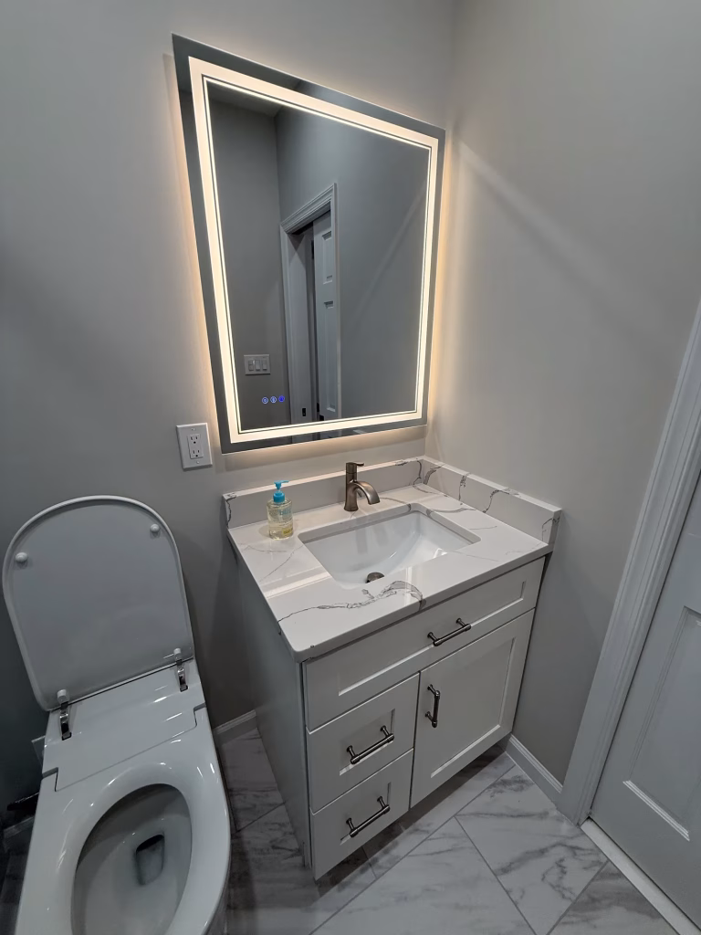 Remodeled bathroom in Arlington, VA with a white shaker vanity, quartz top, LED mirror and marble-look porcelain floor by Kitchen & Bath Masters