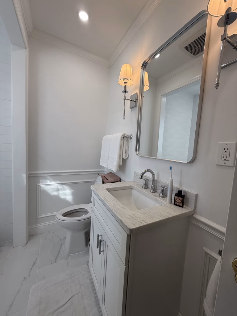 Guest bathroom remodel in Washington, DC with a white shaker vanity, marble-look porcelain floor and wainscoting by Kitchen & Bath Masters