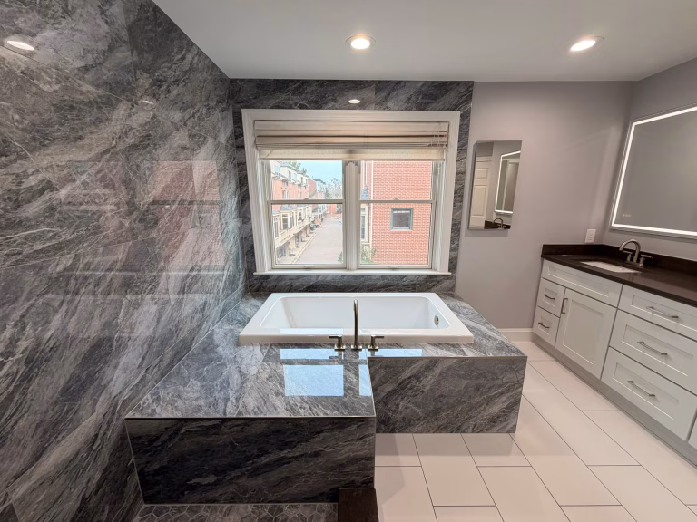 Master bathroom remodel in Arlington, VA with a podium bathtub wrapped in blue-gray marble-look porcelain by Kitchen & Bath Masters
